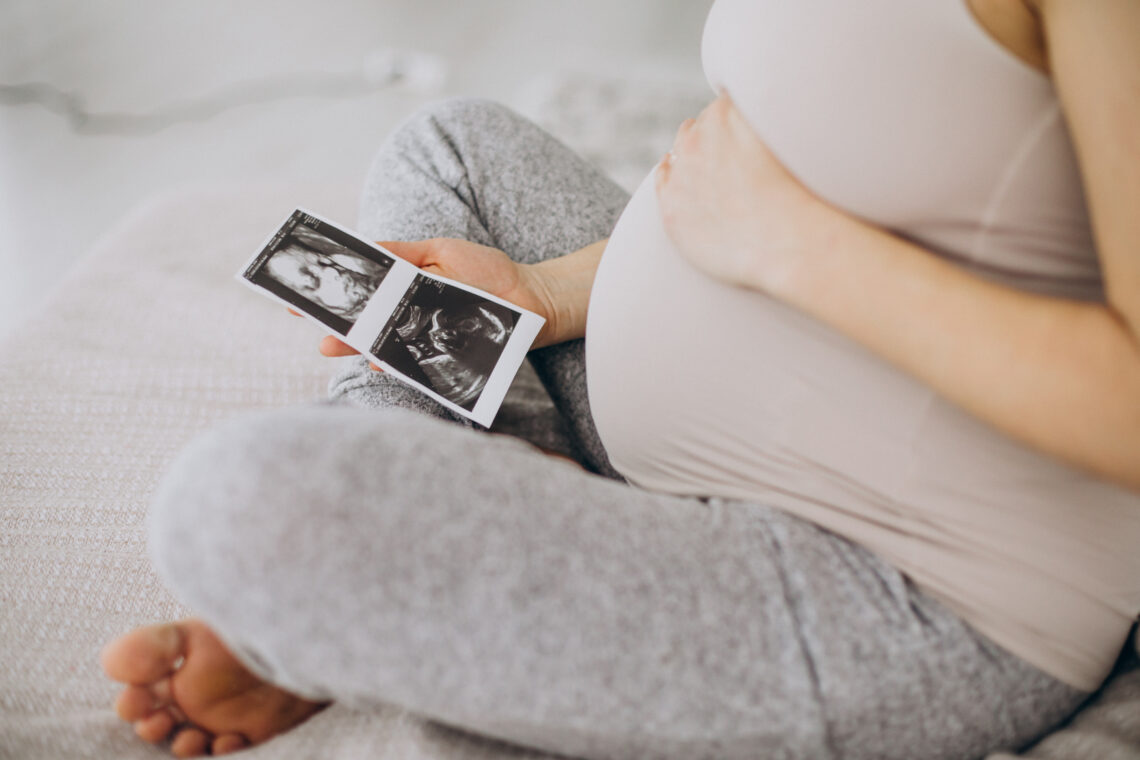 Pregnant woman with ultrasound photo sitting on bed by .