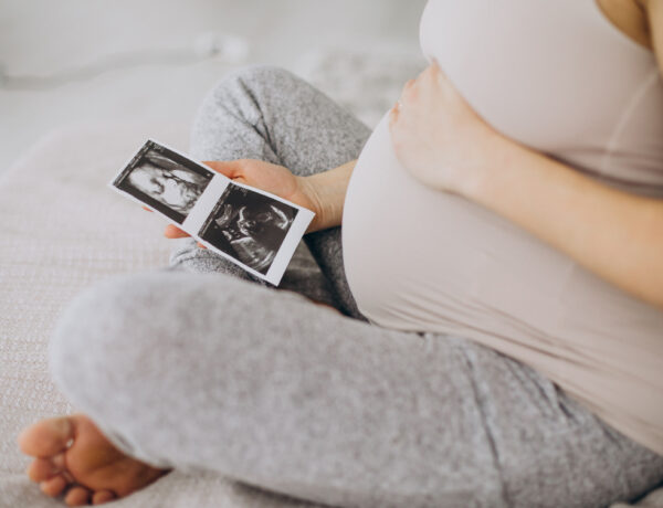Pregnant woman with ultrasound photo sitting on bed by .